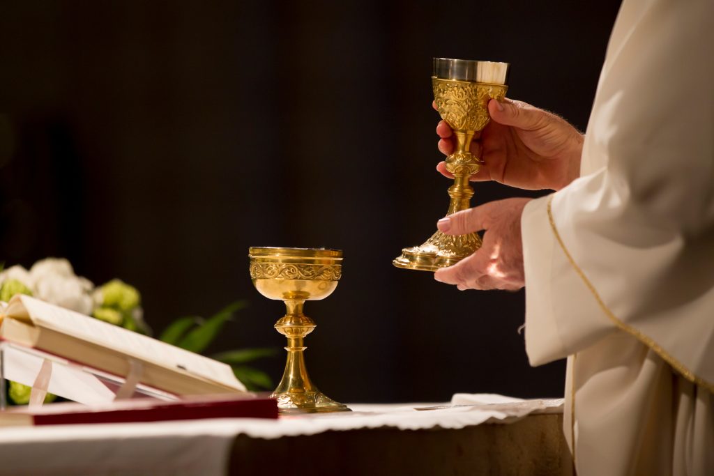 A priest holds a glass of wine to bless it before communion.
